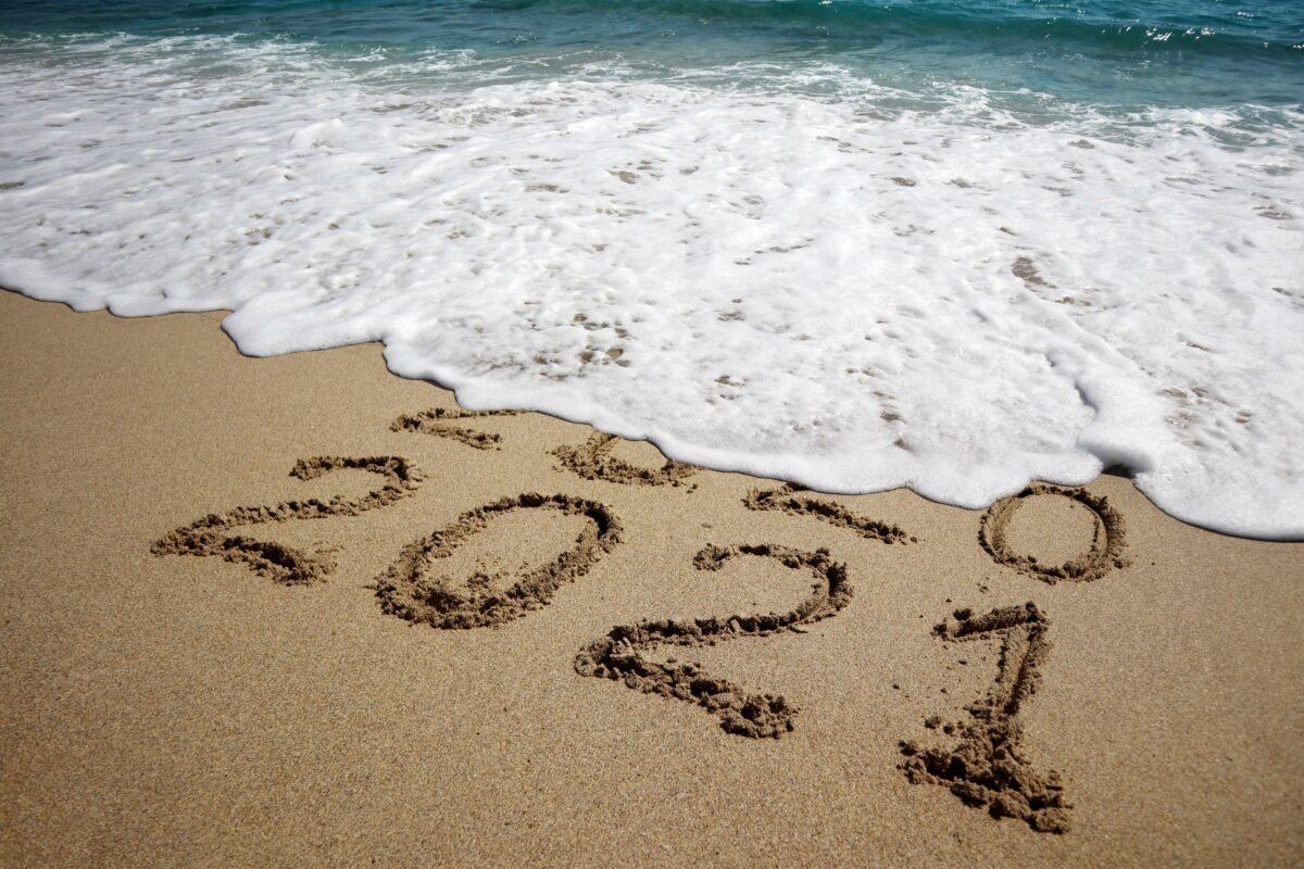 New year 2021 and old year 2020 written on sandy beach with waves. 